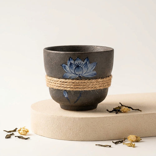 Handcrafted dark ceramic teacup with indigo lotus painting and natural hemp rope wrap
