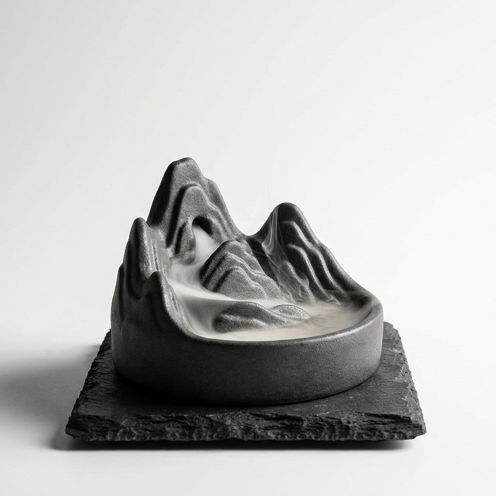 Dark stoneware backflow incense burner with white smoke cascading like mountain fog
